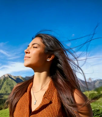 Mental Health - image of a woman standing with hills in the background, and her face directed toward the sun with her eyes closed and wind blowing in her hair giving a light airy feeling of relaxation and freedom.